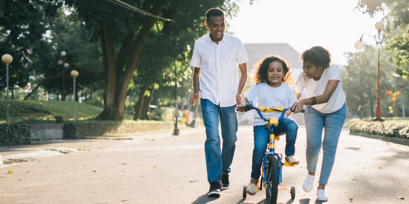 man standing beside his wife teaching their child how to ride bicycle