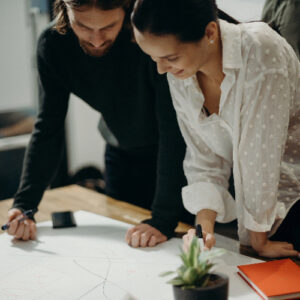 man and woman leaning on table staring at white board on Top of table having a meeting