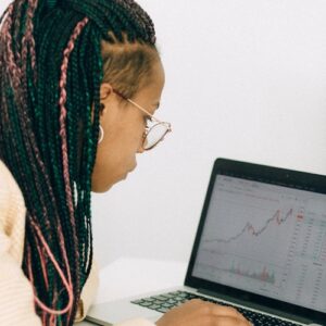 woman in a beige jacket analyzing the graph on her laptop